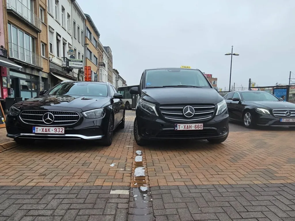 Het wagenpark van ons taxibedrijf, met twee zwarte mercedes busjes voertuigen en een grijze sedan.